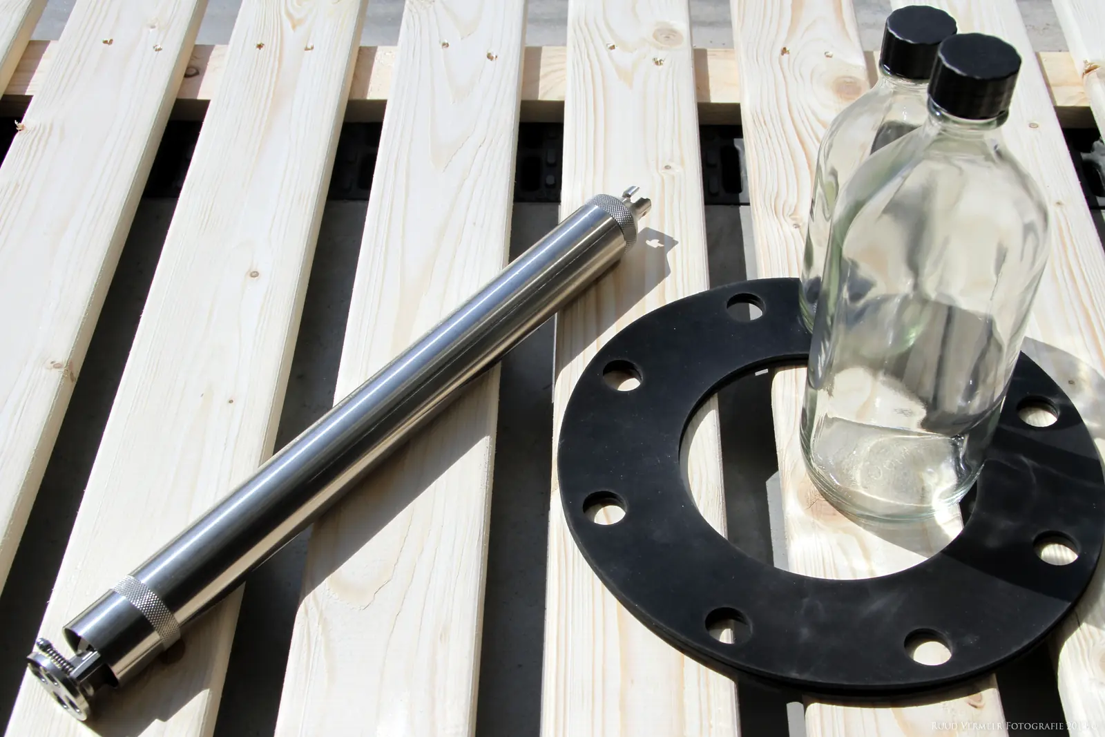 A stainless steel sampler, two glass sample bottles and a flange gasket laid out on a pallet